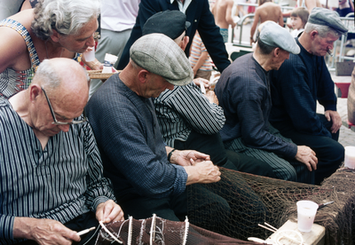 845719 Afbeelding van enkele mannen in klederdracht tijdens het boeten van netten te Spakenburg (gemeente Bunschoten).